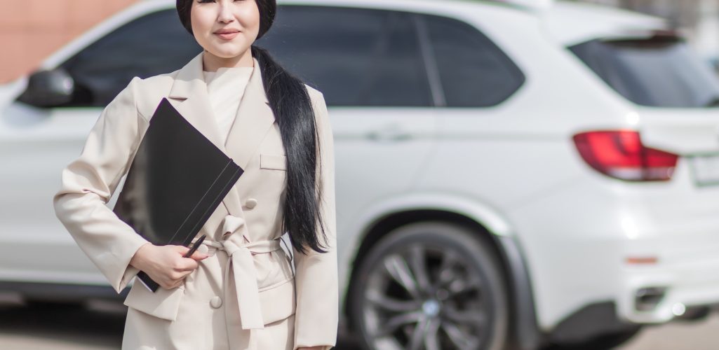 A female insurance agent, wearing a white coat, is holding a folder and a pen for car insurance in Tulsa, OK.