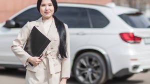 A female insurance agent, wearing a white coat, is holding a folder and a pen for car insurance in Tulsa, OK.