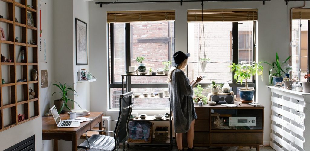 A woman standing in a room with a window of her house thinking about her home insurance.