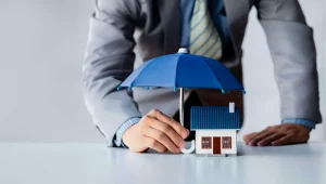 a person holding a small house under a blue umbrella