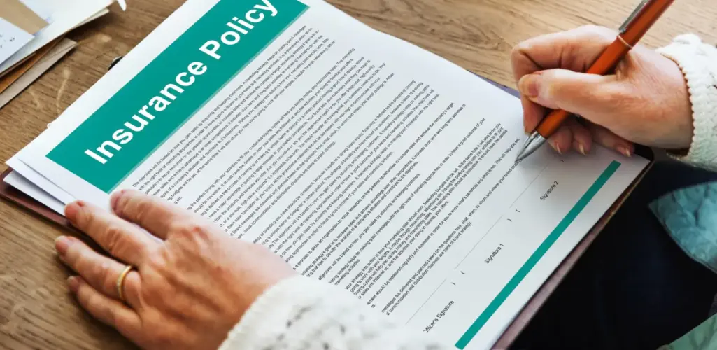 Person signing an insurance document at a desk.