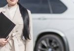 A female insurance agent, wearing a white coat, is holding a folder and a pen for car insurance in Tulsa, OK.